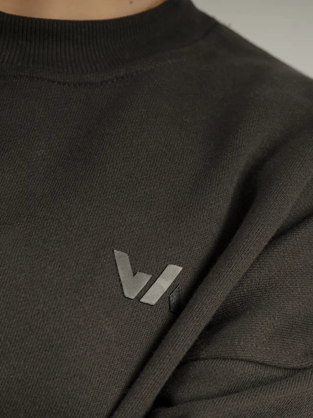 Detalle frontal del crewneck WE ARE color negro, mostrando el logo tonal en el pecho y la textura de la burda de algodón.