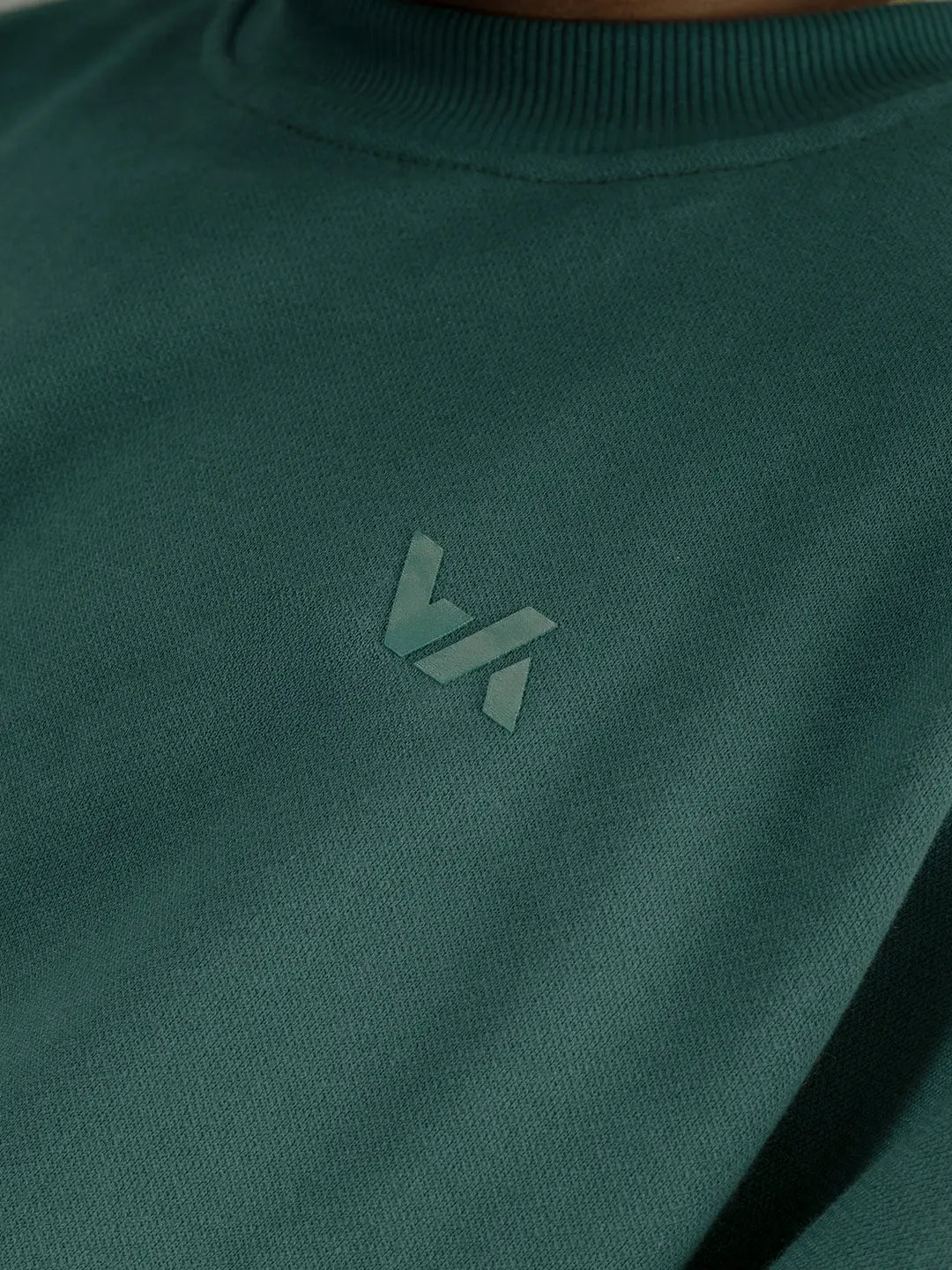 Detalle frontal del crewneck WE ARE color verde, mostrando el logo tonal en el pecho y la textura de la burda de algodón.