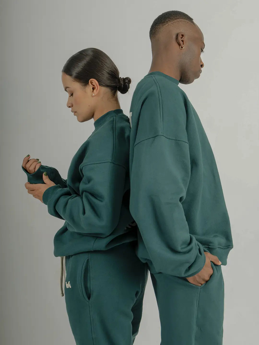 Dos modelos usando crewneck oversized WE ARE color verde con jogger a juego, mostrando la silueta, caída y fit de la prenda.