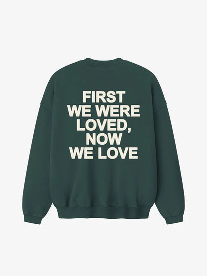 Crewneck oversized WE ARE color verde, vista posterior con estampado “First We Were Loved, Now We Love” en la espalda.