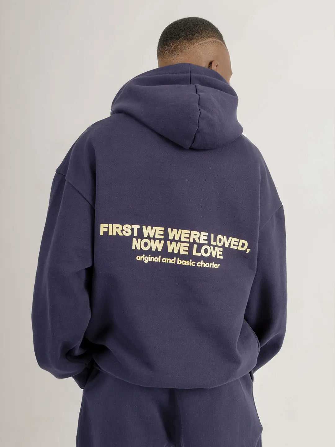 Hoodie oversized WE ARE azul marino, vista posterior con estampado “First We Were Loved, Now We Love”.