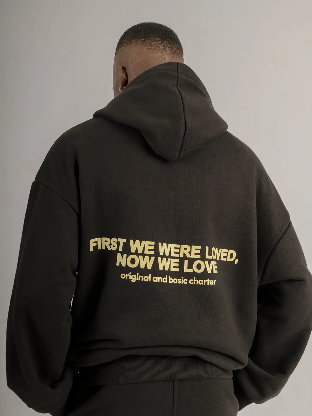 Detalle posterior del hoodie WE ARE negro con estampado “First We Were Loved, Now We Love”.